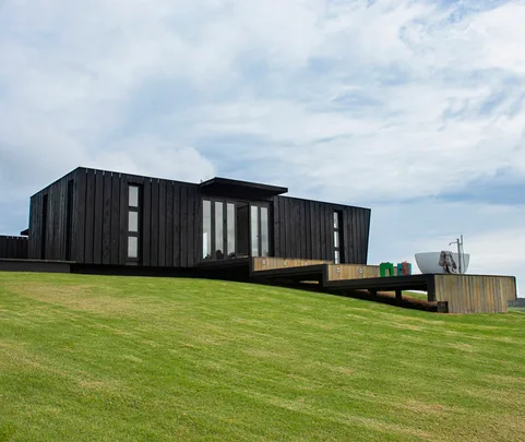Black modern house with sloped lawn and outdoor tub under a cloudy sky.