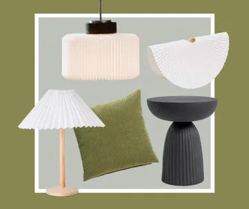 Pendant lamp, table lamp, sculptural object, green cushion, and black side table on olive green background.