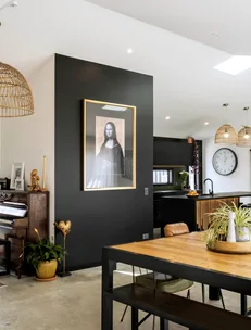 Living room with a large framed Mona Lisa print on a dark wall, wooden dining table, piano, and wicker lights.
