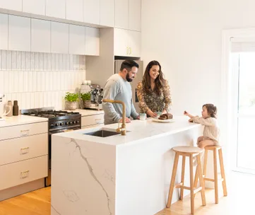 Family in a modern kitchen, preparing a meal. Child sits on a stool at the kitchen island.