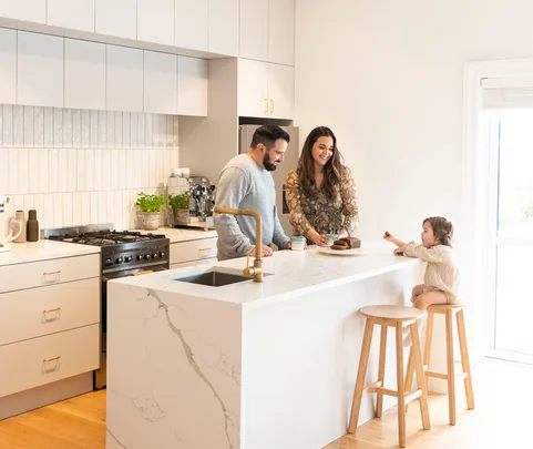 Family in a modern kitchen, preparing a meal. Child sits on a stool at the kitchen island.