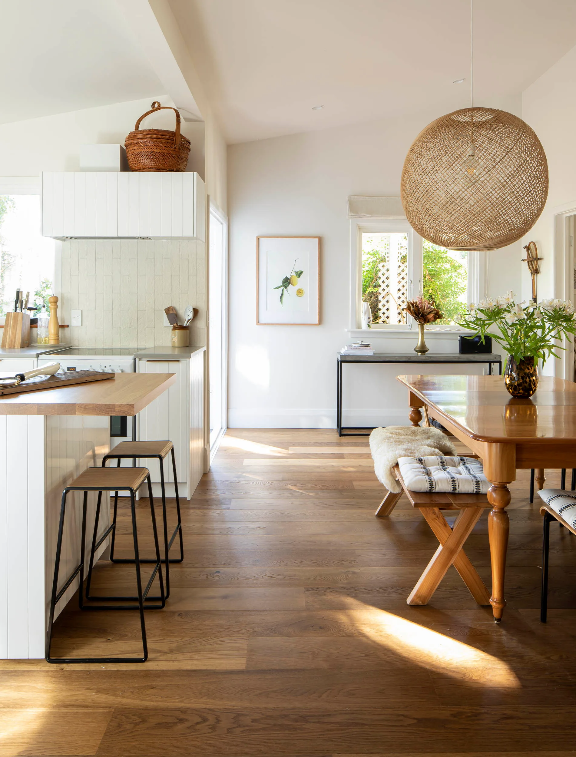 Modern kitchen and dining area with wood floors, bar stools, wicker light fixture, and a table with cushioned bench seating.