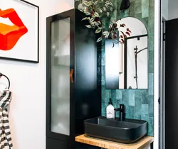 Bathroom with black sink, green tile, round mirror, black cabinet, framed orange lips art, and striped towel.