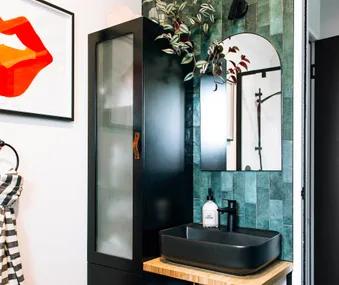 Bathroom with black sink, green tile, round mirror, black cabinet, framed orange lips art, and striped towel.