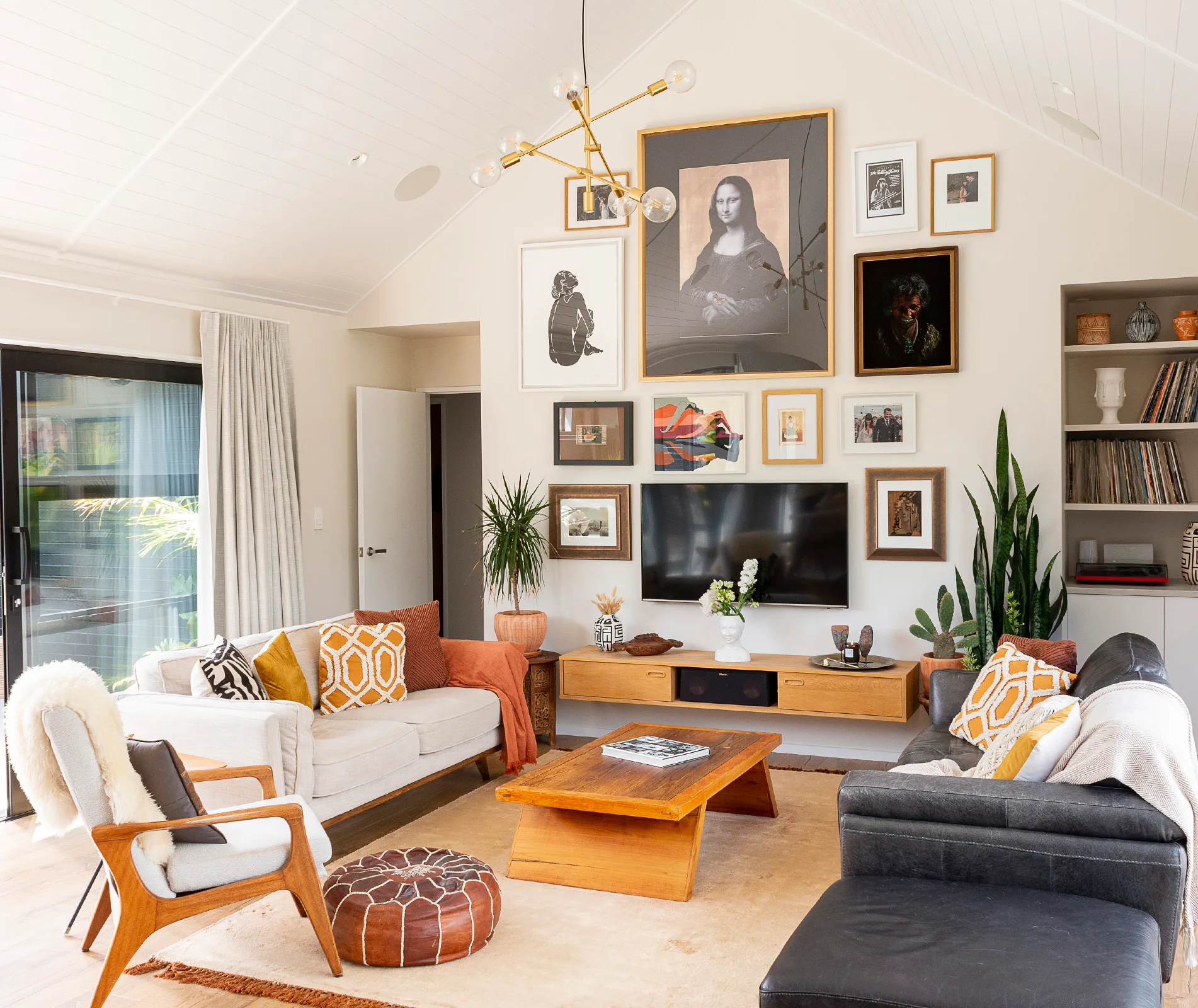 Modern living room with a gallery wall featuring framed art, including the Mona Lisa, beige furniture, and plants.