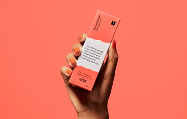 Hand holding Unconditional Skincare Co. Live Probiotic Hydration Serum box against coral background.