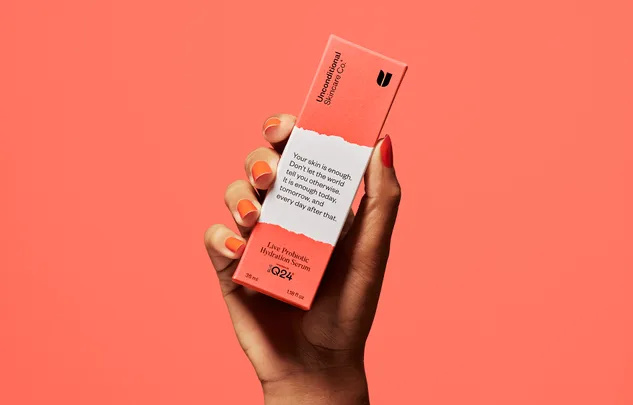 Hand holding Unconditional Skincare Co. Live Probiotic Hydration Serum box against coral background.