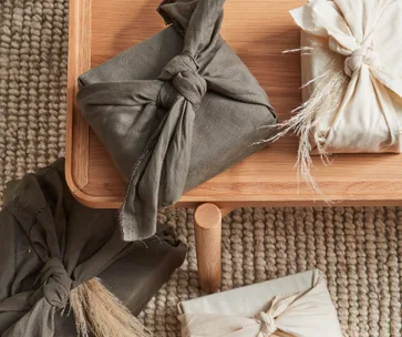 Fabric-wrapped gifts on wooden table, showcasing eco-friendly furoshiki wrapping style, on textured rug background.