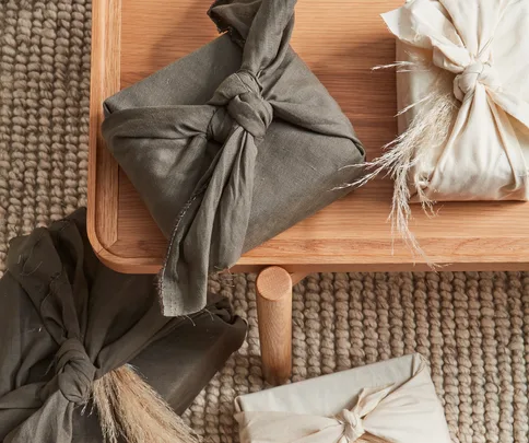 Fabric-wrapped gifts on wooden table, showcasing eco-friendly furoshiki wrapping style, on textured rug background.