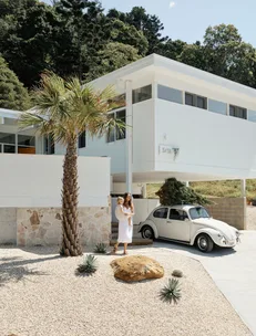 A modern white house with a vintage car and two people near a palm tree.