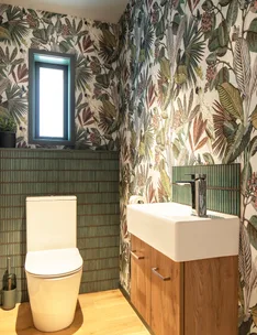 Bathroom with tropical leaf wallpaper, a modern white toilet, and a wooden cabinet with a white sink.
