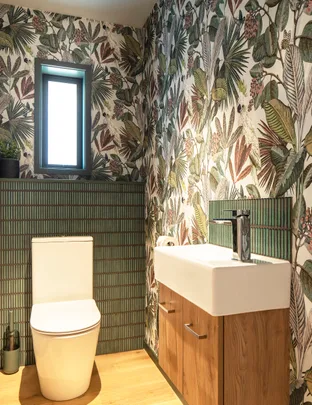 Bathroom with tropical leaf wallpaper, a modern white toilet, and a wooden cabinet with a white sink.