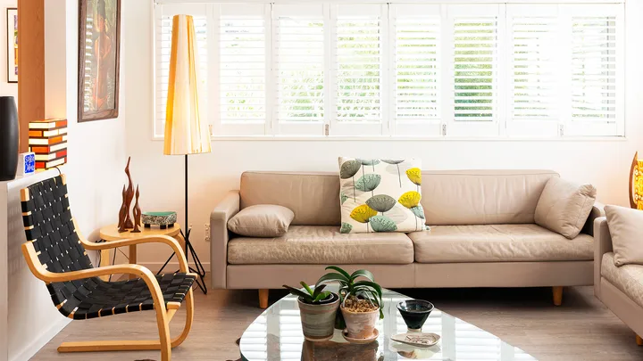 Contemporary living room with beige sofas, a glass coffee table, indoor plants, and a cowhide rug under natural light.