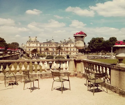 Luxembourg Palace and garden view with empty chairs, ornate urns, and a bright sky.