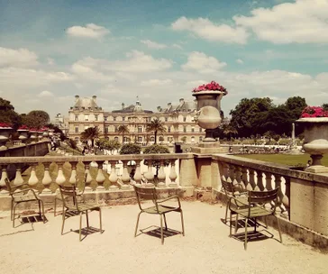 Luxembourg Palace and garden view with empty chairs, ornate urns, and a bright sky.
