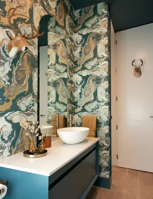 Bathroom with marble-patterned wallpaper, white vessel sink, and antler decor on the wall.