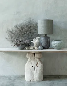 Decorative console table with driftwood base, featuring a lamp, vases, and dried plants against a neutral wall.