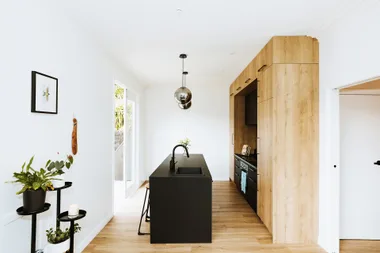 Modern kitchen with wooden cabinets, black island, pendant lights, and indoor plants.