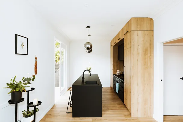 Modern kitchen with wooden cabinets, black island, pendant lights, and indoor plants.