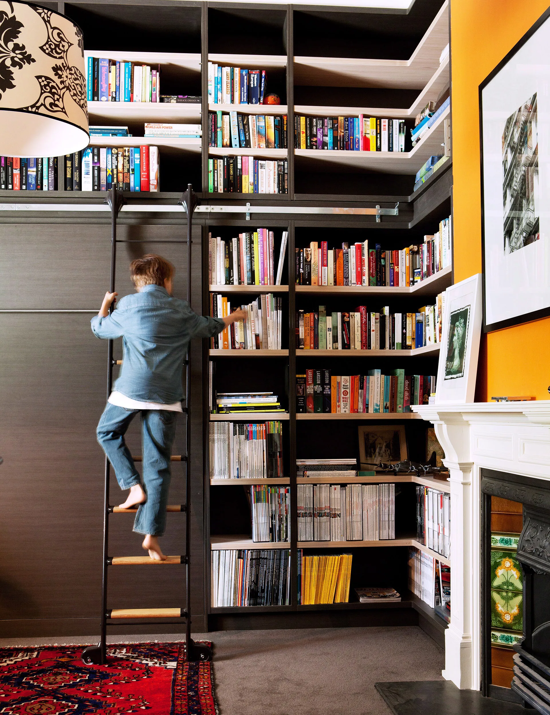A person climbing a ladder to reach a large bookshelf filled with books in a cozy living room.