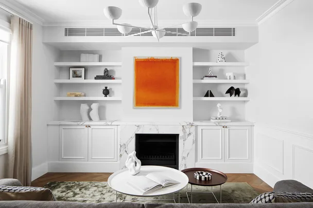 Bright living room with white decor, shelves, an orange painting, and a marble fireplace.
