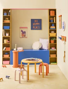 Bright playroom with colorful stools, toys, and books; sign reads "My Happy Place," art of zebra, and "Be Kind" decor.