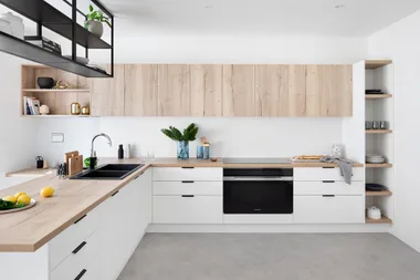 Modern kitchen with wooden cabinets, black sink, and open shelving, featuring lemons and green plants on the counter.