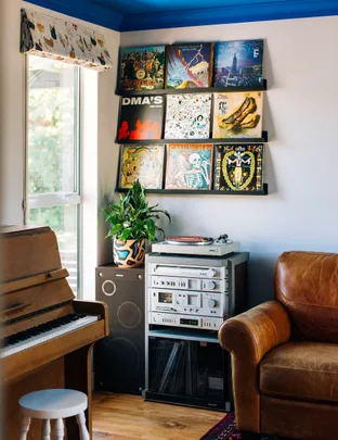 Vinyl records on shelves, vintage stereo, piano, and leather couch in cozy room.