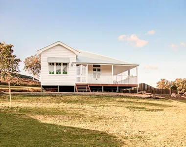 White wooden house with a porch, on green grass under a clear blue sky.