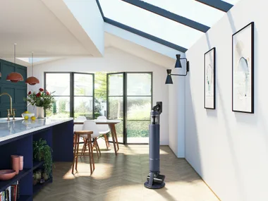 Modern kitchen with a vacuum cleaner on the wooden floor, large windows, blue cabinets, and stylish decor elements.