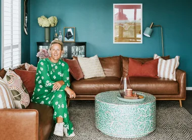 A person in a green floral dress sits on a brown sofa in a stylishly decorated living room.