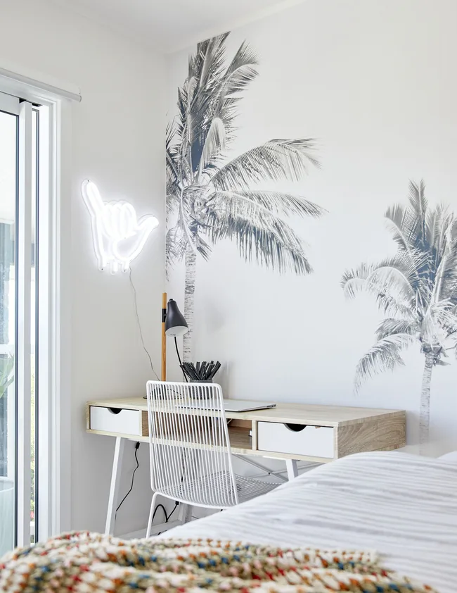 Contemporary bedroom with desk, chair, palm tree mural, and a neon shaka hand sign on the wall.