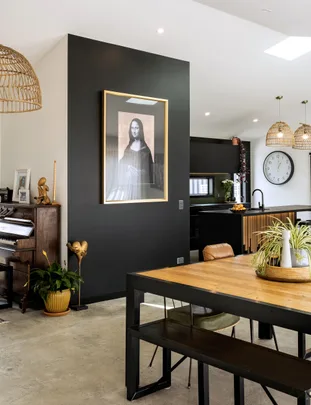 Modern kitchen with a framed Mona Lisa print on a black wall, wooden dining table, and hanging wicker lights.