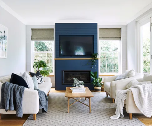 Stylish living room with navy accent wall, modern fireplace, and beige sofas arranged around a wooden coffee table.