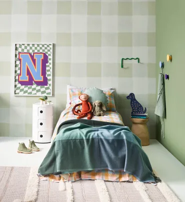 A child's bedroom with a single bed, toys, patterned bedding, wall decor, and green walls.