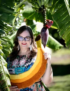 Person holding a large banana-shaped rug standing among banana trees.
