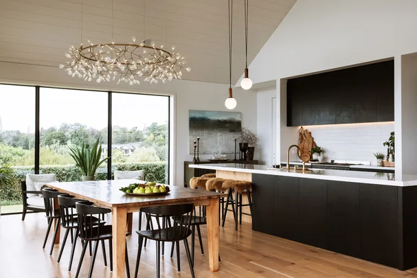 Modern kitchen and dining area with wooden table, black chairs, large windows, and decorative lighting fixture.