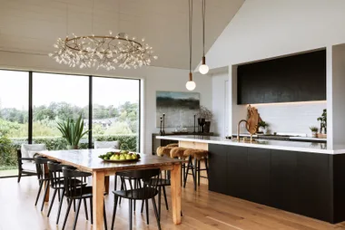 Modern kitchen and dining area with wooden table, black chairs, large windows, and decorative lighting fixture.