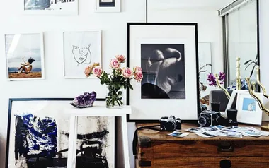 Artistic home decor with framed prints, vintage cameras, and pink roses on a wooden table.
