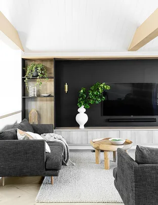 Modern living room with black sofa, wood table, plants, white vase, and wall-mounted TV on black accent wall.