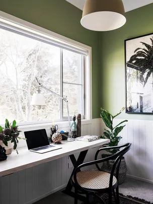 Bright home office with a green wall, desk, chair, laptop, and plants by a window.