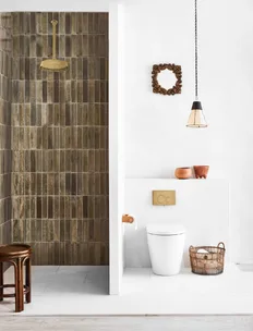 Stylish bathroom with a tiled shower, white toilet, wicker basket, wooden stool, hanging lamp, and decorative mirror.