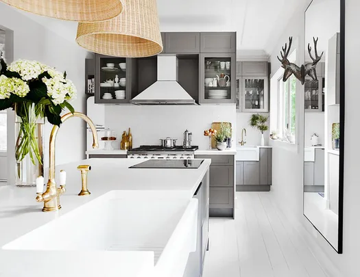 Modern kitchen with white countertops, brass faucet, gray cabinets, and decor including flowers and a deer head wall mount.