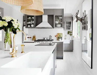 Modern kitchen with white countertops, brass faucet, gray cabinets, and decor including flowers and a deer head wall mount.
