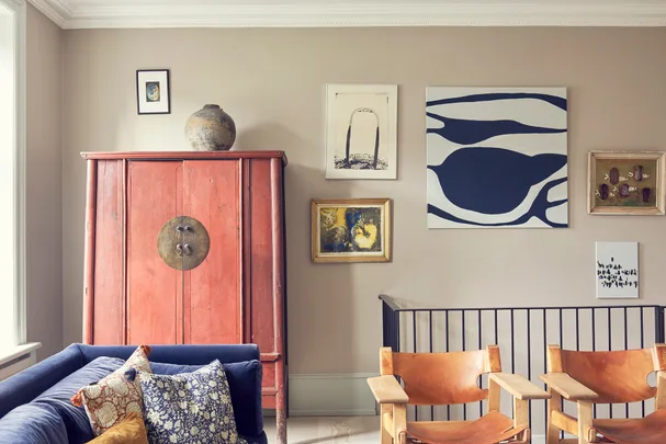 A stylish living room with a red cabinet, blue sofa, patterned cushions, wall art, and wooden chairs.