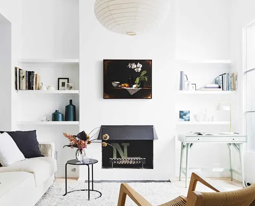 Stylish living room with modern decor, white walls, a fireplace, art, a sofa, shelves with books, and a small table.