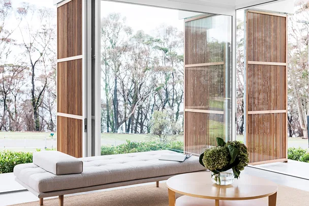 Modern living room with daybed, large glass doors, and wooden shutters overlooking a garden view.