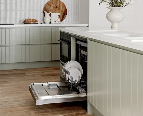 Kitchen with green cabinets, a dishwasher with open door showing dishes, and counter with decor and bread.
