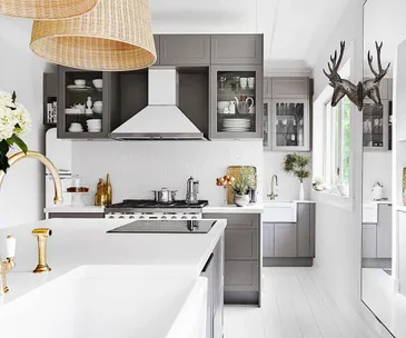 Modern kitchen with gray cabinets, white countertops, gold fixtures, wicker lampshades, and antler wall decor.