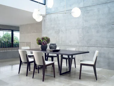 Modern dining area with six white chairs, a dark rectangular table, gray vases, and a concrete textured wall.